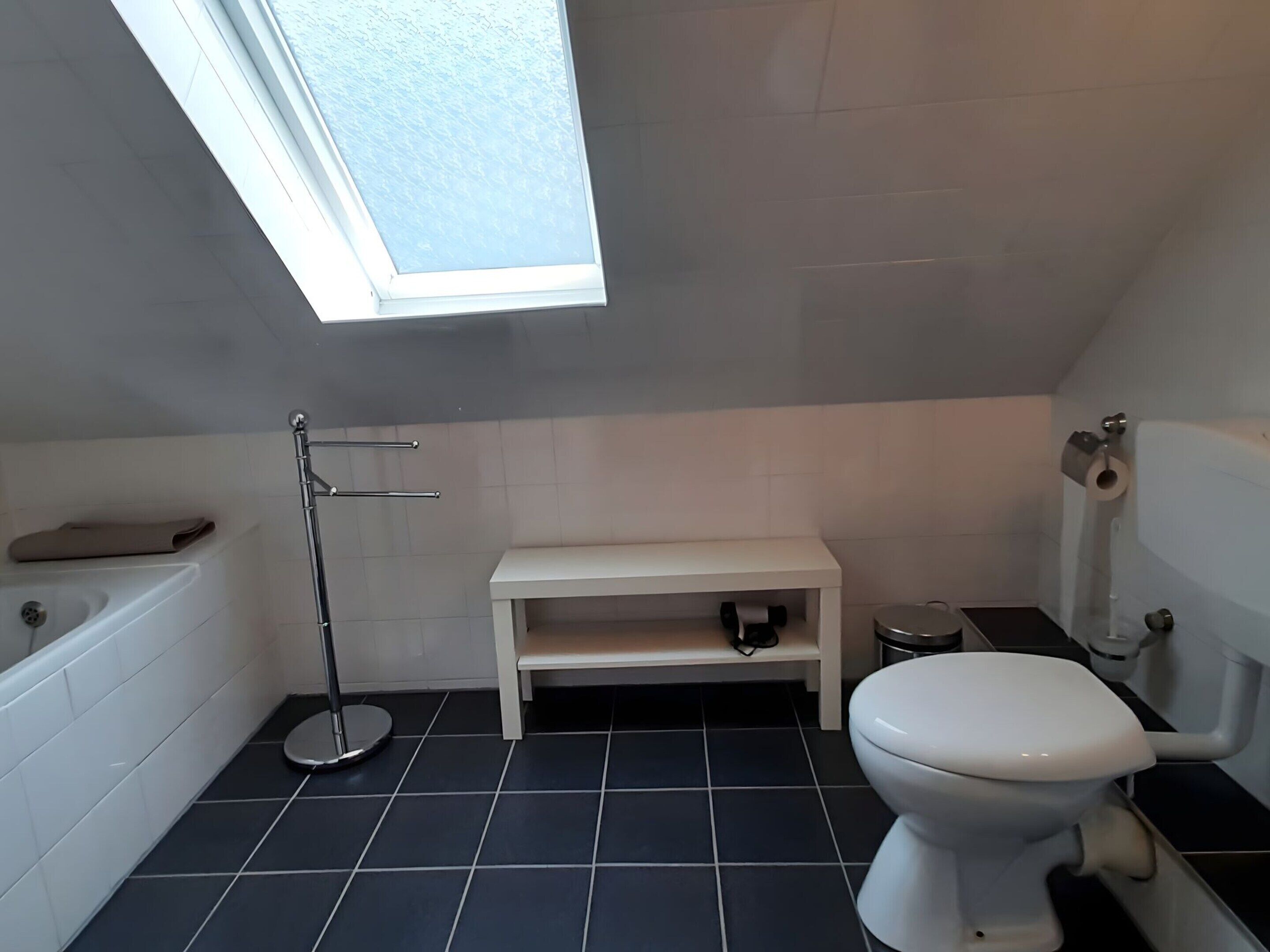 Ein Badezimmer mit Badewanne, Toilette und einem kleinen weißen Regal.