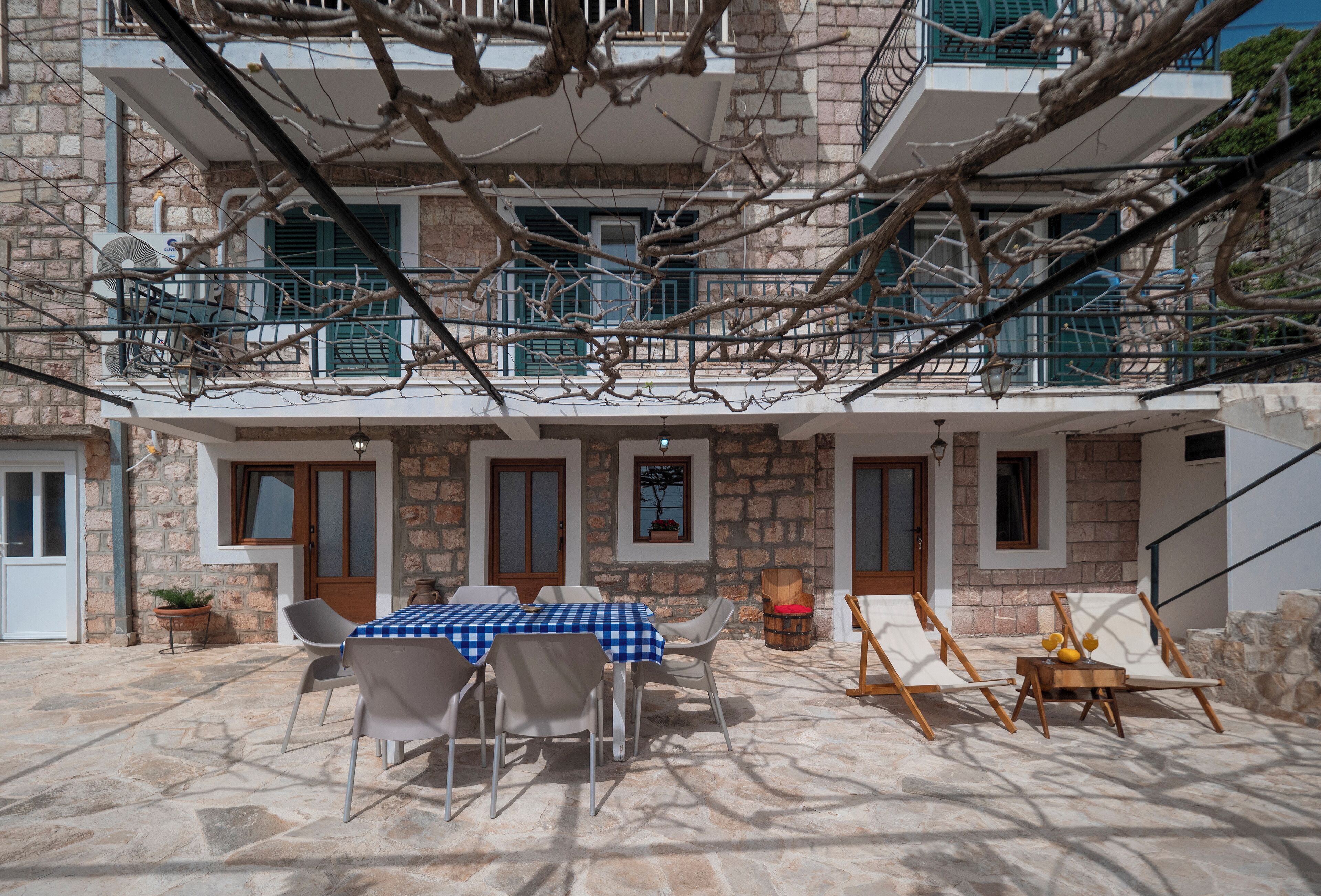 A stone building with a balcony, outdoor seating, and a table with a checkered tablecloth.