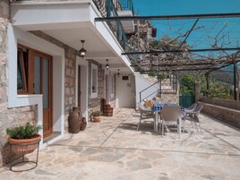 Un patio con suelo de piedra, mobiliario exterior, una escalera y vistas del paisaje circundante.
