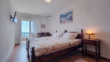 Une chambre avec un lit en bois, une table de chevet avec une lampe, un tableau au mur et une vue sur la mer par la fenêtre.