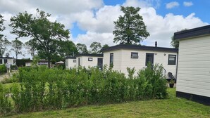 A row of mobile homes with a grassy yard and trees in the background. - Cozy Chalet on a Holiday Park Near Alkmaar (Hensbroek)
