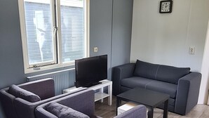 A living room with a grey sofa, two armchairs, a coffee table, and a TV on a white stand. - Cozy Chalet on a Holiday Park Near Alkmaar (Hensbroek)