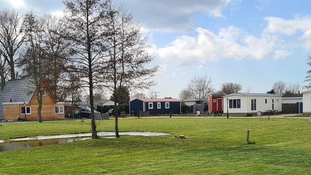 A residential area with houses, a grassy field, and a small pond. - Cozy Chalet on a Holiday Park Near Alkmaar (Hensbroek)
