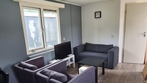 A living room with a grey sofa, two armchairs, a coffee table, and a TV on a white stand. - Cozy Chalet on a Holiday Park Near Alkmaar (Hensbroek)