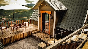 A wooden deck with a bench and table, a small wooden building with a sloped roof, and a view of a green landscape in the background. - Ayliya Bungalow (Akçaabat)