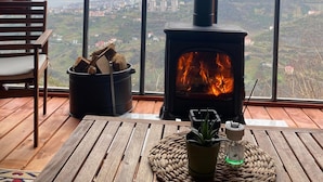 A cozy room with a large window, a wooden table, a chair, a fireplace, and a view of a cityscape. - Ayliya Bungalow (Akçaabat)