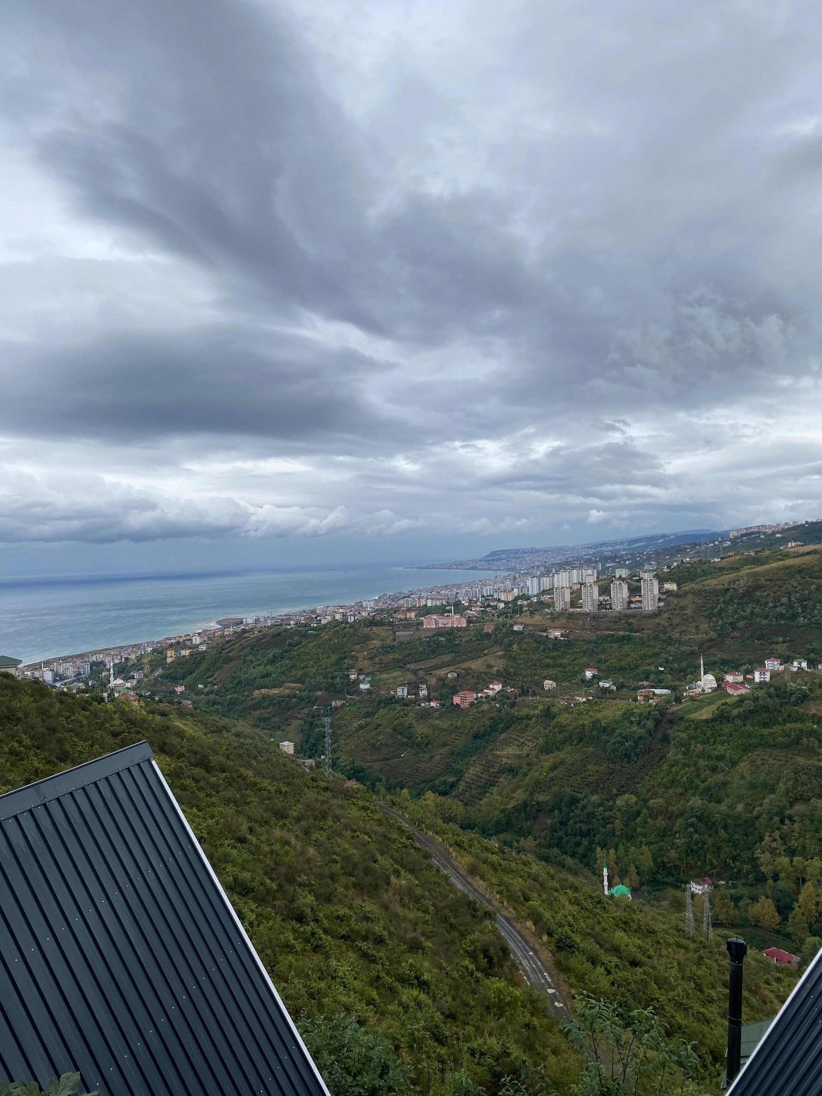 A coastal cityscape with a view of the sea and a hilly terrain.