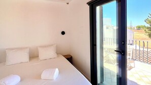 Een slaapkamer met een bed, kussens, een nachtkastje en een grote schuifglazen deur die leidt naar een buitenruimte.
