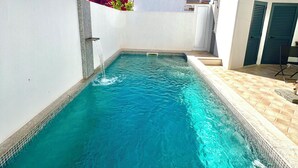 Een zwembad met helderblauw water, omgeven door witte muren en een betegeld zonnedek.