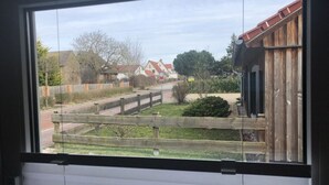 Blick aus einem Fenster auf eine Straße mit Häusern, einem Holzzaun und einem kleinen Garten.