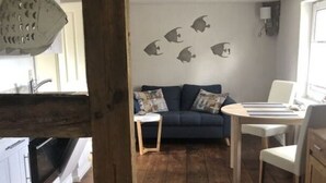 Ein gemütlicher Wohnbereich mit Holzboden, einem blauen Sofa, einem weißen Tisch und einer Küche mit weißen Schränken und einem Herd.