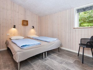A room with two beds, a chair, and a window with a view of greenery.