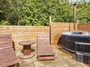 An outdoor patio with wooden furniture, including a table and two lounge chairs, and a hot tub.