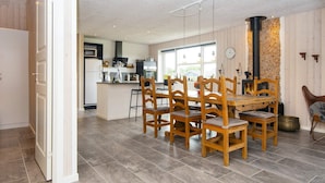 A spacious kitchen with modern appliances, a dining area with wooden chairs, and a stone wall with a fireplace. - 5 Star Holiday Home in Hemmet (Hemmet)