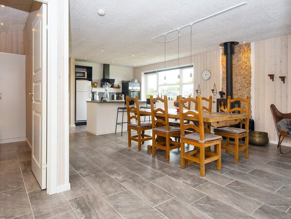 A spacious kitchen with modern appliances, a dining area with wooden chairs, and a stone wall with a fireplace. - 5 Star Holiday Home in Hemmet (Hemmet)