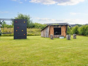 A climbing wall and a rustic wooden structure with a door, set in a grassy area with trees and shrubs in the background.