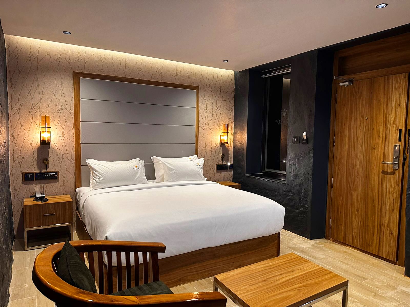 Ein modernes Hotelzimmer mit einem großen Bett, Nachttischen, einem Holzstuhl und einem kleinen Tisch.