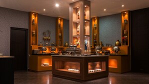 A modern hotel lobby with a central reception desk, wooden shelving with decorative items, and a dark-toned floor. - Viceroy Luxury Mountain Resort (Udumbanchola)