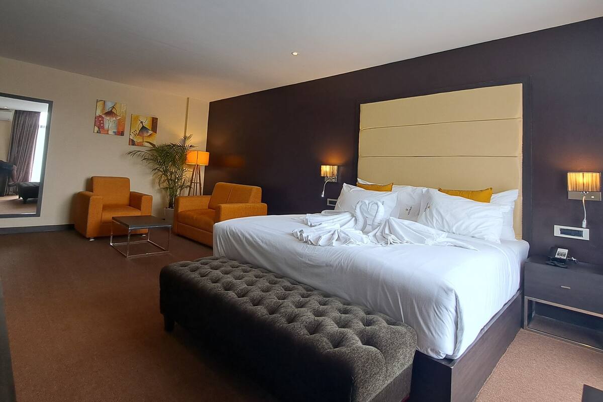 Una habitación de hotel moderna con una cama grande, dos sillones, una mesita y un espejo amplio.