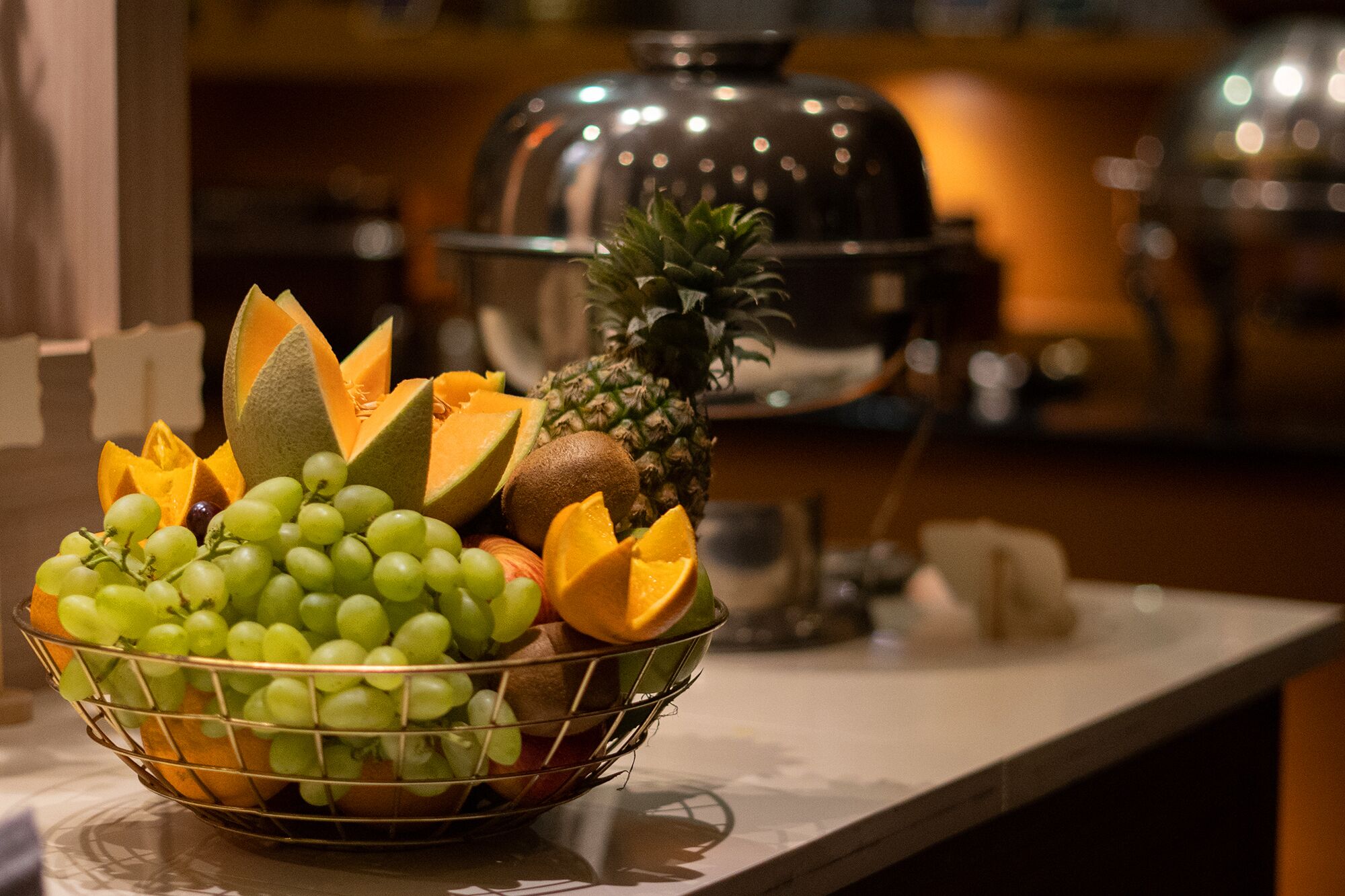A fruit bowl with grapes, pineapple, and melon on a kitchen counter.