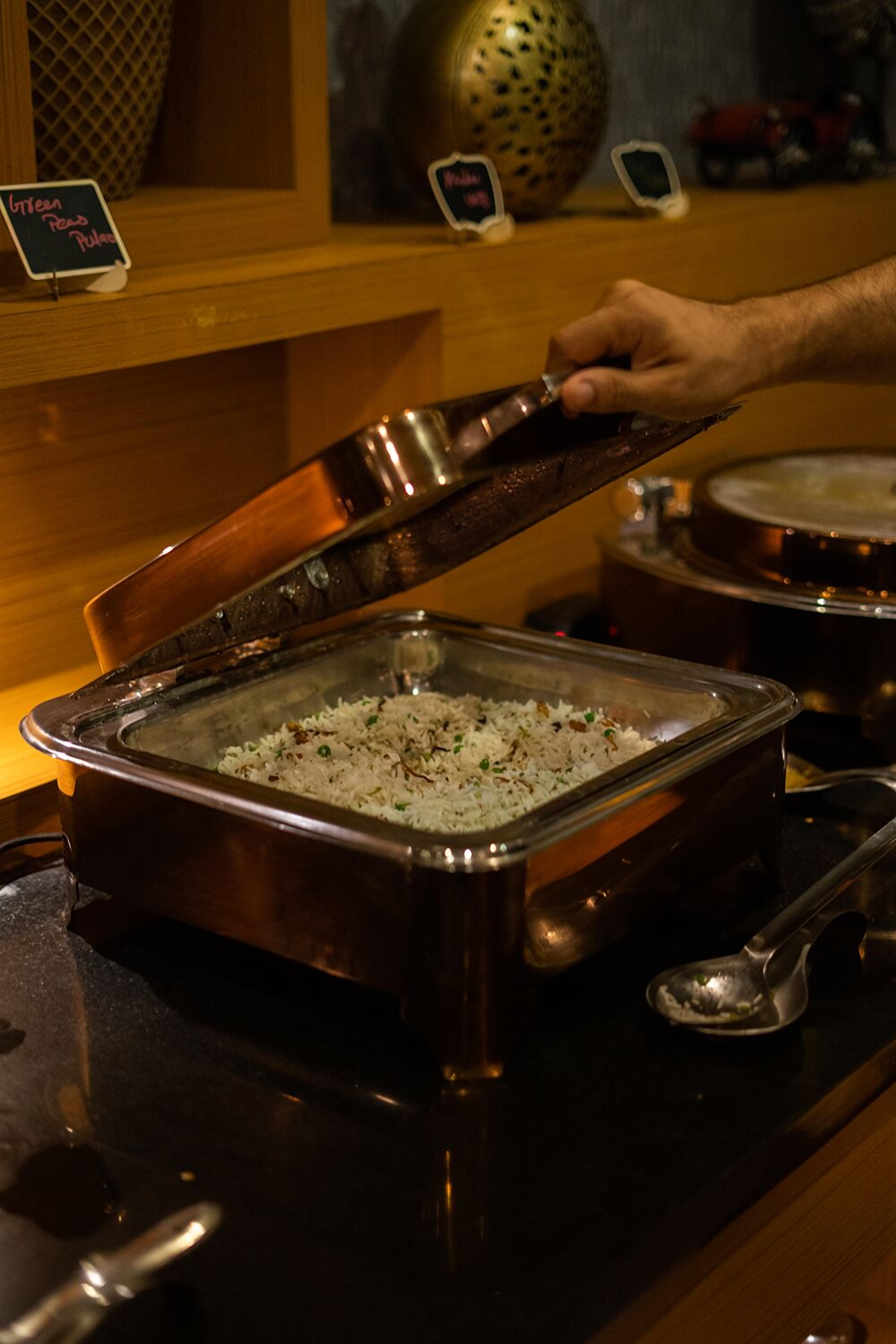 Disposição de buffet com uma mão levantando a tampa de um recipiente cheio de arroz.