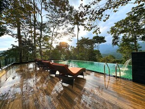 A wooden deck with lounge chairs overlooking a pool, surrounded by trees and a mountainous landscape. - Viceroy Luxury Mountain Resort (Udumbanchola)