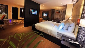 A modern hotel room with a large bed, a TV mounted on the wall, a desk with a computer, and a potted plant. - Viceroy Luxury Mountain Resort (Udumbanchola)
