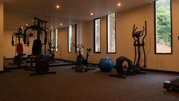 A gym with various exercise equipment, large windows, and a carpeted floor.