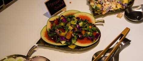 A variety of dishes including a salad in a watermelon bowl, a fruit salad, and a green salad with a sign indicating 'Green Salad'.