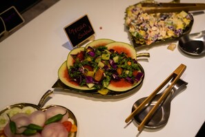 Verschiedene Gerichte, darunter ein Salat in einer Wassermelonen-Schale, Obstsalat und ein grüner Salat mit dem Hinweis 'Grüner Salat'.