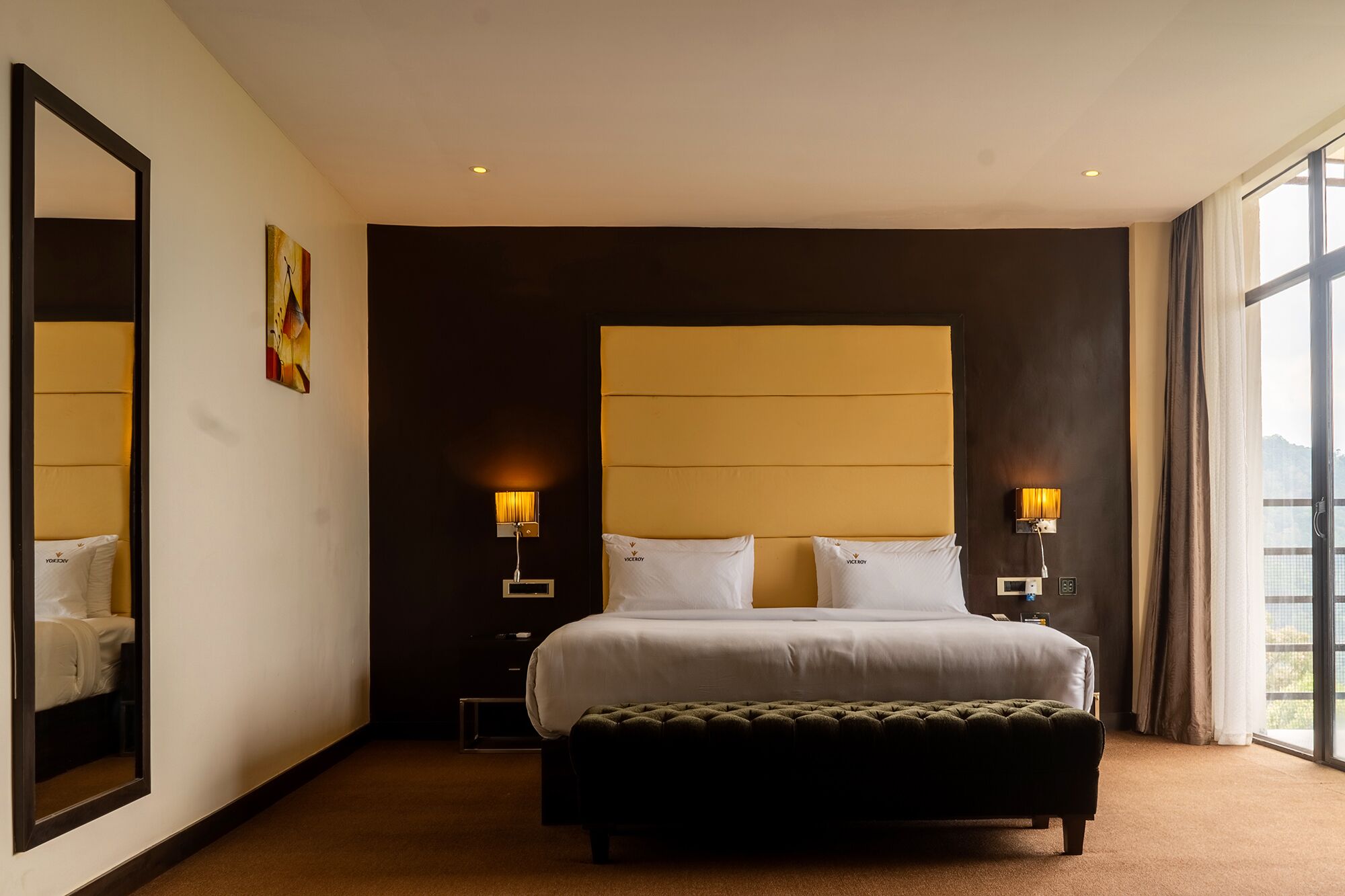 Hotelkamer met een groot bed, twee bedlampen, een nachtkastje, een spiegel en een raam met uitzicht.
