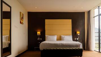 Hotelkamer met een groot bed, twee bedlampen, een nachtkastje, een spiegel en een raam met uitzicht.