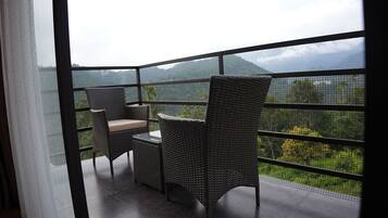 Un balcón con mobiliario de mimbre y una mesa de vidrio, con vistas a un paisaje montañoso.