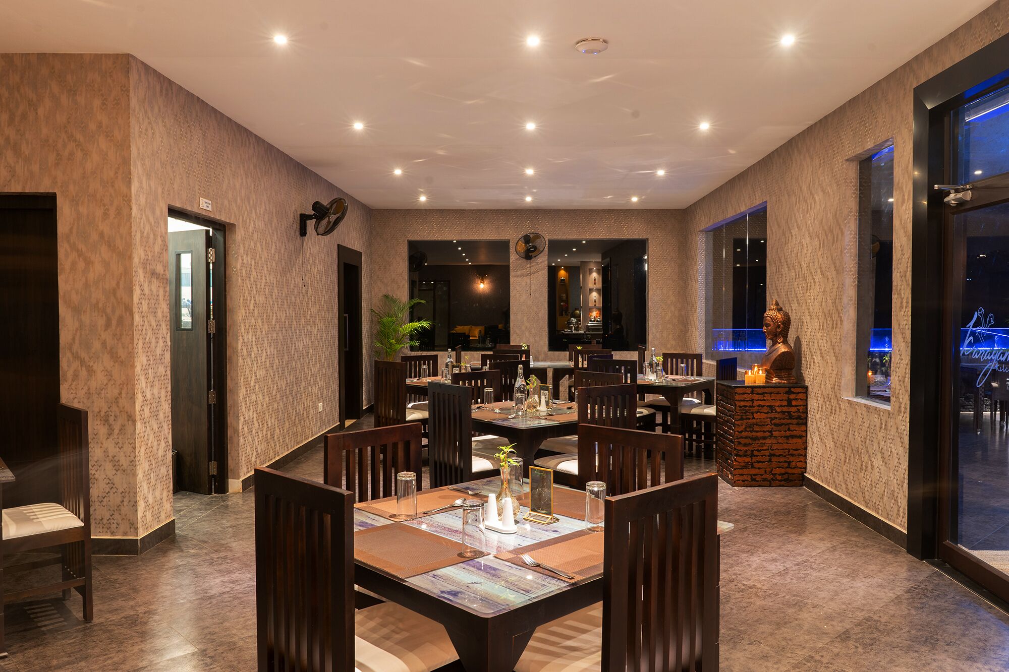 A restaurant with multiple tables, chairs, and a Buddha statue.