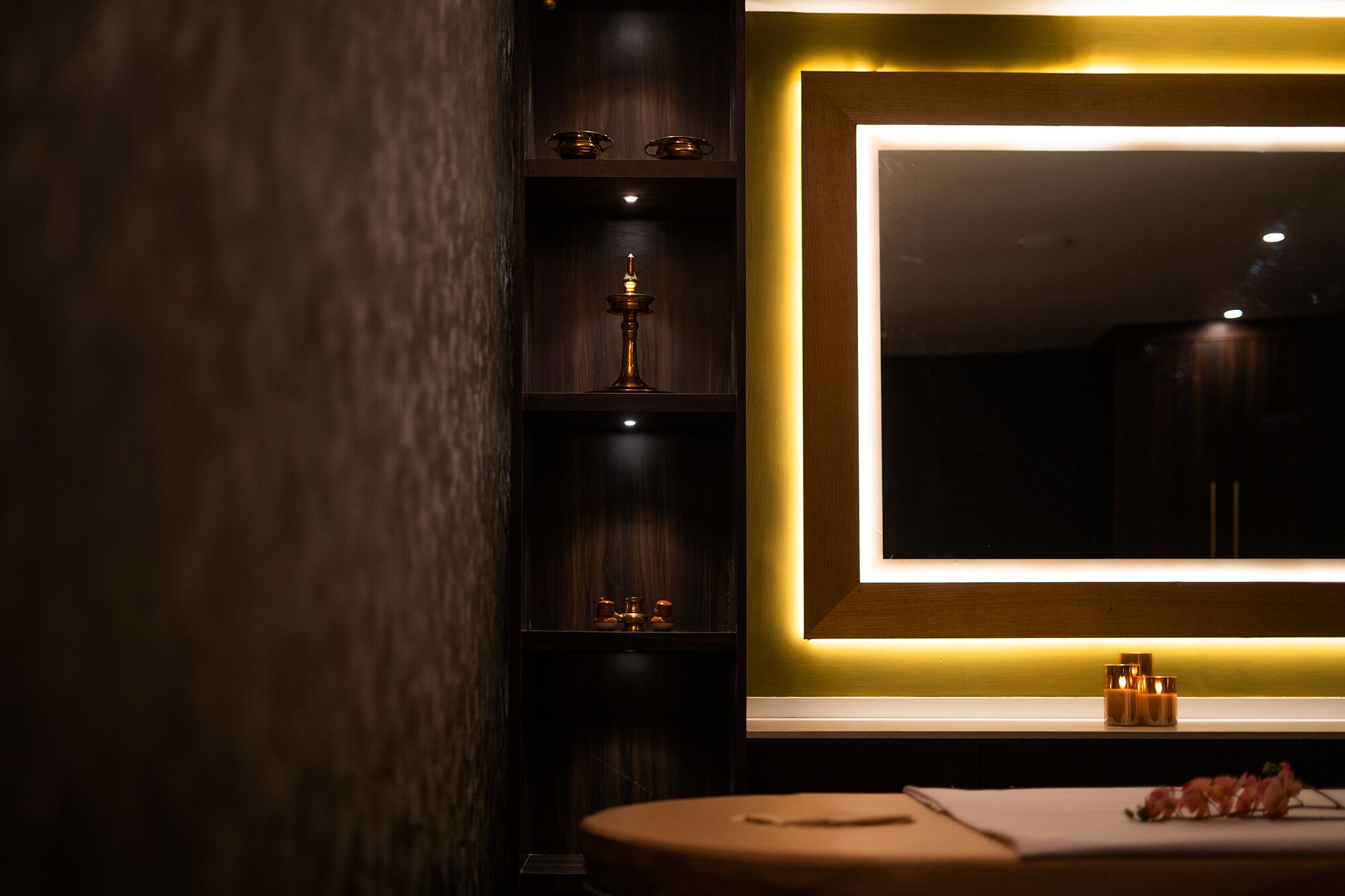 Un baño moderno con muebles de madera oscura, un espejo grande y una mesita redonda con una toalla y una botella.