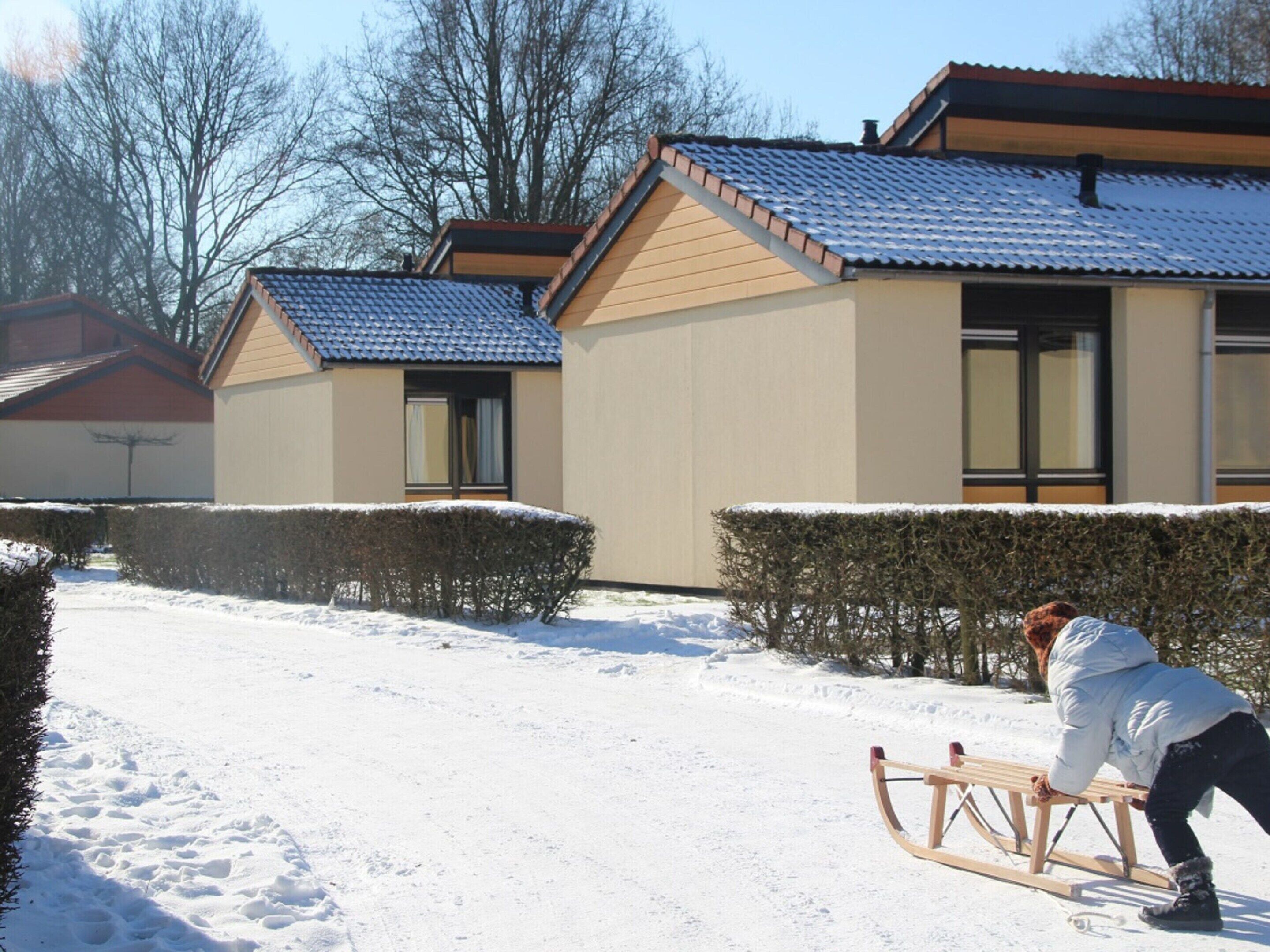 Un sentier enneigé mène à une maison avec un toit bleu et des murs de couleur beige.