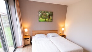 Ein Doppelbett mit weißer Bettwäsche, zwei Nachttische mit Lampen, ein Baumgemälde an der Wand und ein großes Fenster mit Vorhängen.