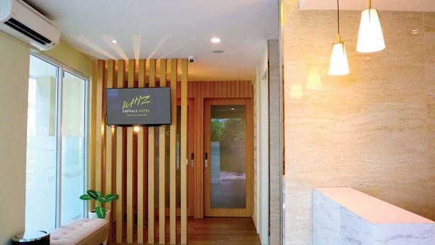 A reception area with a TV screen displaying 'Wiz Capsule Hotel' and a wooden slatted wall. - Whiz Capsule Thamrin Jakarta (Jakarta)