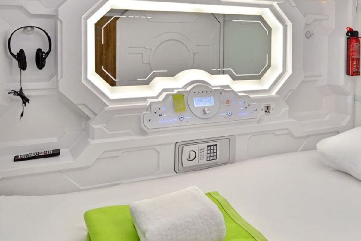 Habitación de diseño futurista, que incluye un panel de control, auriculares y una almohada verde.