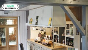 Zona de bar con taburetes, una barra y estanterías llenas de botellas.