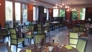 Un restaurante con mesas redondas, sillas verdes y una araña.