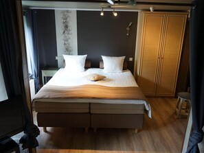 A neatly made bed with white bedding and two pillows, a wooden wardrobe, and a small stool.