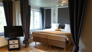 Un dormitorio con cama, televisor sobre un mueble y ventana con cortinas.