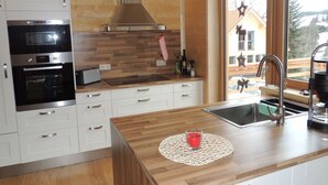 A modern kitchen with wooden cabinetry, stainless steel appliances, and a large window offering a view of the outside. - Huttenzauber 1 Comfortable Holiday Residence (Annaberg-Lungoetz)