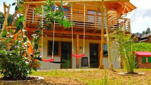 A wooden cabin with a balcony, a swing set, and a small garden area. - Huttenzauber 1 Comfortable Holiday Residence (Annaberg-Lungoetz)