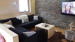 A cozy living room with a black sofa, a wooden coffee table, and a stone wall. - Huttenzauber 1 Comfortable Holiday Residence (Annaberg-Lungoetz)