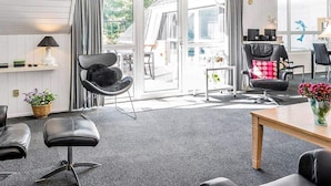 A modern living room with a black leather sofa, a wooden table, and a dining area with a black chair.