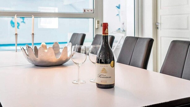 A table with a bottle of wine, two glasses, and a decorative metal bowl in a modern room with a view of the sea.