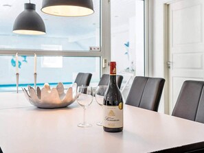 Ett bord med en vinflaska, två glas och en dekorativ metallskål i ett modernt rum med utsikt över havet.