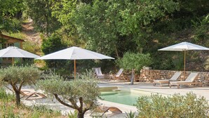 Ein Poolbereich mit Liegestühlen und Sonnenschirmen, umgeben von Bäumen und einer Steinmauer.